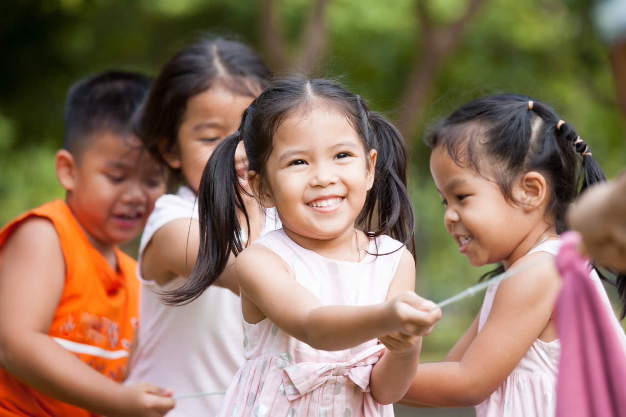 a child is playing with her friends happily because her parents teach her about social interaction skills