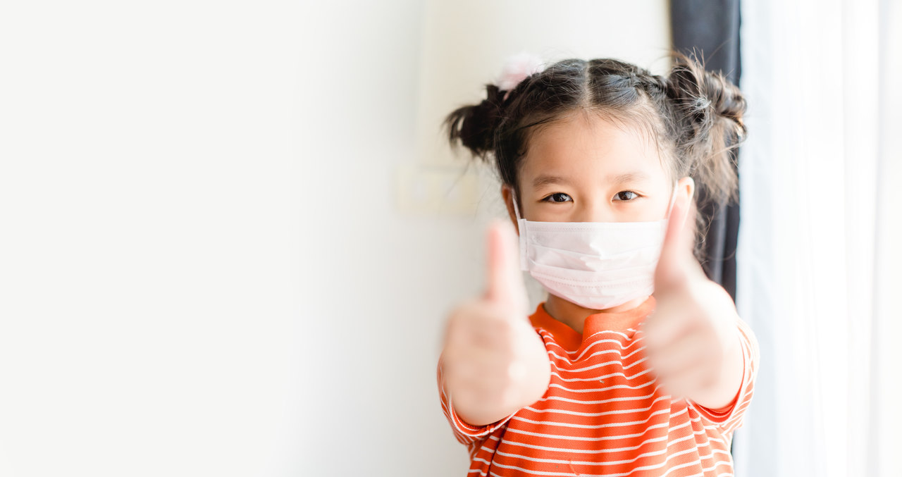 a child is showing her thumb while wearing a mask in a new normal era