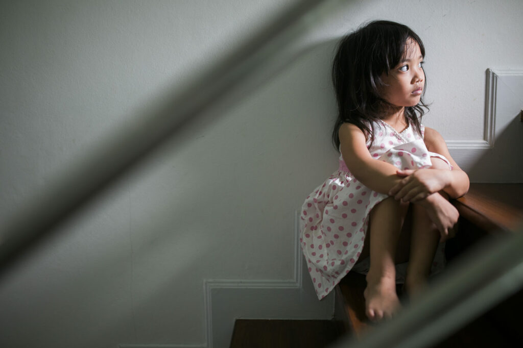 A child is suffering with her troubled childhood that affects her mental health. She is sitting on a stair and staring at the wall.
